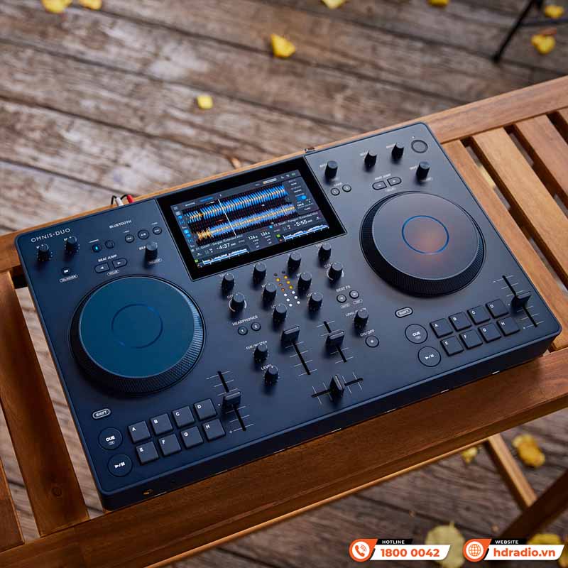 Omnis-Duo đặt trên nền gỗ, hiển thị màn hình trung tâm với waveform và thông tin track, hai jog wheel lớn.